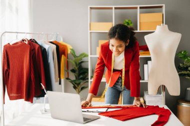 Sakin, kıvırcık esmer, koyu tenli kadın modern moda tasarımcısı, dizüstü bilgisayar ve tablet bilgisayarın ofisinde.