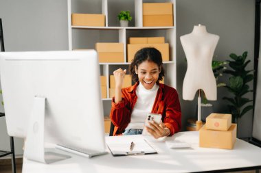 Genç işletme sahibi Afrikalı kadın paket kutuları hazırlıyor ve online siparişleri kontrol ediyor..