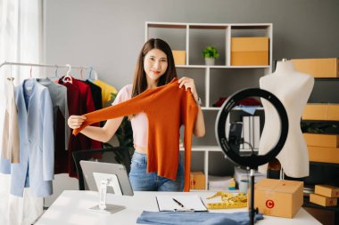 Moda blogcusu konsepti, genç Asyalı kadın video yayınında kıyafet satıyor. Akıllı telefon ve tablet kullanarak küçük işletme KOBİ 'si kurun.