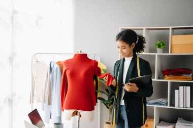 Sakin, kıvırcık esmer, koyu tenli kadın modern moda tasarımcısı, dizüstü bilgisayar ve tablet bilgisayarın ofisinde.