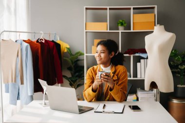 Sakin, kıvırcık esmer, koyu tenli kadın modern moda tasarımcısı, dizüstü bilgisayar ve akıllı telefonun ofisinde..