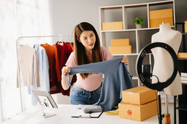 Moda blogcusu konsepti, genç Asyalı kadın video yayınında kıyafet satıyor. Akıllı telefon ve tablet kullanarak küçük işletme KOBİ 'si kurun.