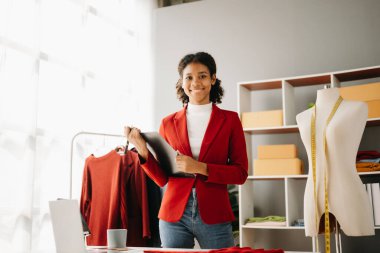 Sakin, kıvırcık esmer, koyu tenli kadın modern moda tasarımcısı, dizüstü bilgisayar ve akıllı telefonun ofisinde..