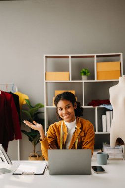 Sakin, kıvırcık esmer, koyu tenli kadın modern moda tasarımcısı, dizüstü bilgisayar ve akıllı telefonun ofisinde..