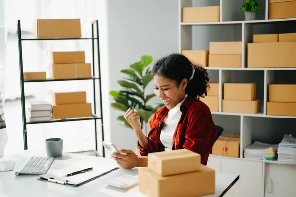 stock image Young business owner African woman prepare parcel boxes and  check online orders for deliver to customer on computer, Shopping Online concept.