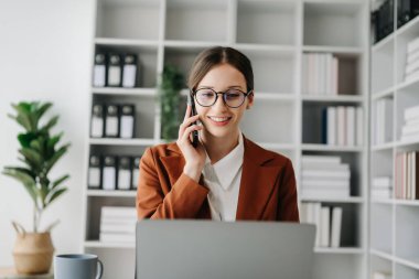 İş kadını beyaz kadın telefonda konuşuyor ve ofiste dizüstü bilgisayar kullanıyor.