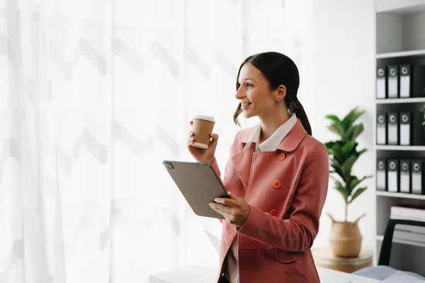 Confident businesswoman with digital tablet and coffee in creative office