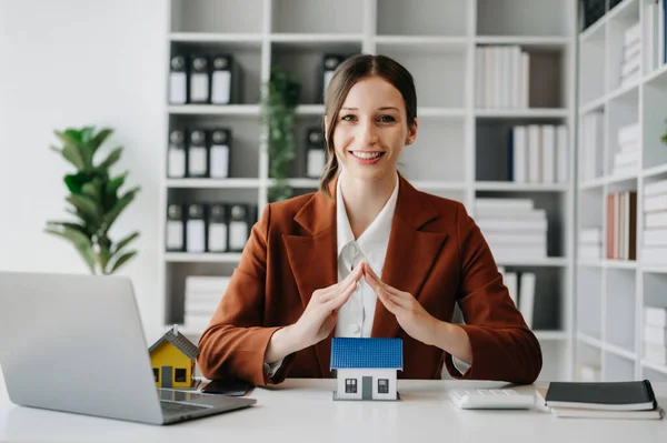 Beyaz kadın emlakçı ev alım satımı, ofis masasında satın alma gibi emlak yatırımları için çatıyı korumak için elleri kullanıyor.