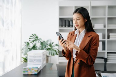 Asyalı iş kadını modern ofiste telefon kullanıyor.