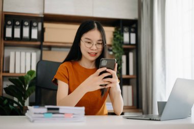 Ofiste dizüstü bilgisayar ve telefonla çalışan Asyalı bir iş kadını.