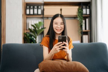  Kanepede oturan Asyalı kız oturma odasındaki telefonu kullanıyor.