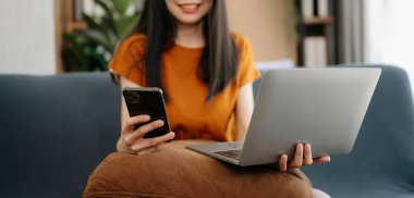 Evde akıllı telefon ve dizüstü bilgisayar kullanan bir kadın