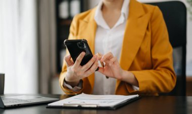 Bilgisayarda çalışan kendine güvenen bir iş kadını ve modern ofisindeki iş yerinde akıllı telefon..