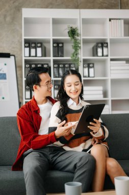 İki Asyalı öğrenci evdeki oturma odasındaki kanepede tabletle birlikte online olarak öğreniyor.