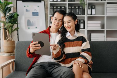 İki Asyalı öğrenci evdeki oturma odasındaki kanepede tabletle birlikte online olarak öğreniyor.