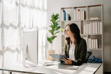 Modern ofiste elinde tabletle gülümseyen kendine güvenen bir kadın.