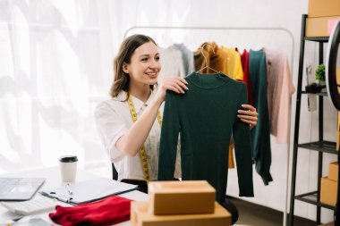 Asyalı terzi kadın terzi atölyesinde giysiler üzerinde çalışıyor. Güzel genç bayan moda tasarımcısı ofiste.