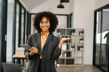 Modern ofiste elinde tabletle gülümseyen kendinden emin bir Afrikalı kadın.