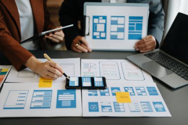  UX geliştiricisi ve ui tasarımcısı modern ofiste müşteri özeti ve renk kodu ile mobil uygulama arayüzü kablo tasarımı hakkında beyin fırtınası yapıyorlar