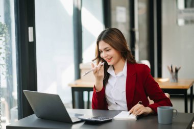 İş kadını Asyalı kadın telefonda konuşuyor ve ofiste otururken bilgisayarını gülümsüyor.
