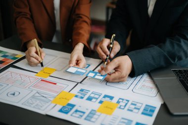  UX geliştiricisi ve ui tasarımcısı modern ofiste müşteri özeti ve renk kodu ile mobil uygulama arayüzü kablo tasarımı hakkında beyin fırtınası yapıyorlar