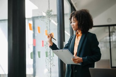 Gökdelendeki modern ofiste çalışan bir sekreter ve pencere modern ofisindeki görevlere yapışkan notlar yapıştırıyor.