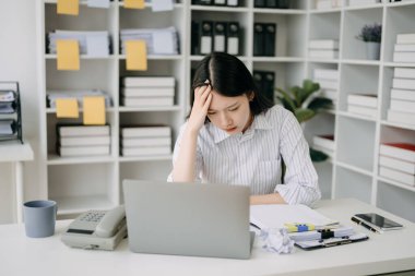 Asyalı kadın migren ağrısı çekiyor. Ofiste dizüstü bilgisayarla çalışırken çok çalışan iş kadını finansörü..