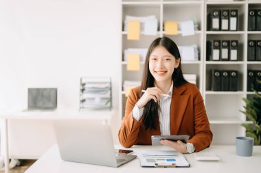 Tablet ve dizüstü bilgisayarlı çekici bir Asyalı kadın evinden modern ofise bakıyor. 