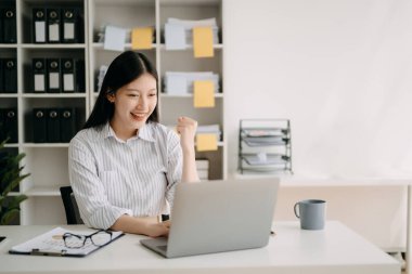 Asyalı iş kadını, modern ofiste dizüstü bilgisayarla çalışan mutlu ve mutlu biri.