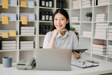 Ofiste çalışan Asyalı iş kadını, modern ofiste tablet ve dizüstü bilgisayarla çalışıyor.