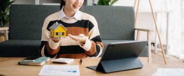 Emlak komisyoncusu ev modeli ile tablet bilgisayardaki karar alma tablosu sigorta sözleşmesini sunar ve müşteriye danışmanlık yapar.