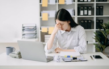 Asyalı kadın migren ağrısı çekiyor. Ofiste dizüstü bilgisayarla çalışırken çok çalışan iş kadını finansörü..