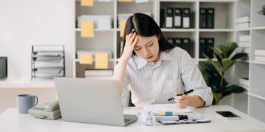 Asyalı kadın migren ağrısı çekiyor. Ofiste dizüstü bilgisayarla çalışırken çok çalışan iş kadını finansörü..