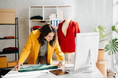 Kafkasyalı genç bir kadın, ofisinde bilgisayar ve tabletle moda tasarımcısı.