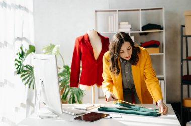 Kafkasyalı genç bir kadın, ofisinde bilgisayar ve tabletle moda tasarımcısı.