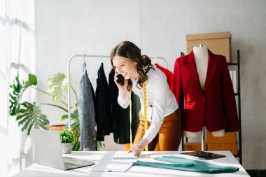Modern stüdyoda dizüstü bilgisayarı ve telefonu olan moda tasarımcısı kadın. 