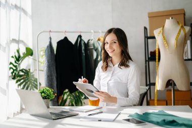 Modern stüdyoda dizüstü bilgisayarı ve dijital tableti olan moda tasarımcısı kadın. 