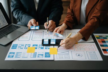  UX geliştiricisi ve ui tasarımcısı modern ofiste müşteri özeti ve renk kodu ile mobil uygulama arayüzü kablo tasarımı hakkında beyin fırtınası yapıyorlar