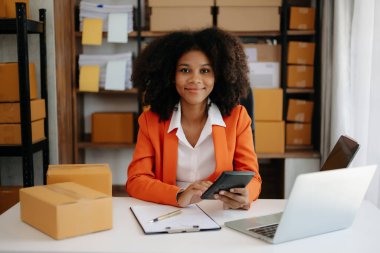 Başlangıçta küçük işletme KOBİ 'si, Girişimci sahibi Afrikalı kadın dizüstü bilgisayar kullanıyor ve paket ürün kutularını hazırlamak için online alışveriş siparişlerini kontrol ediyor. ev ofisinde.