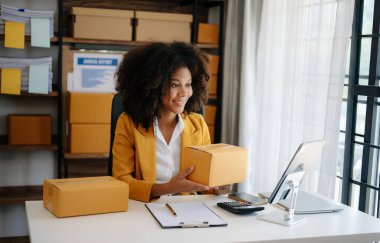 Küçük işletme girişimcisi KOBİ Serbest çalışan Afrikalı kadın evde tablet bilgisayar ve kutularla çalışıyor