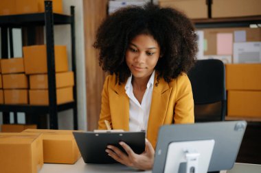 Küçük işletme girişimcisi KOBİ Serbest çalışan Afrikalı kadın evde tablet bilgisayar ve kutularla çalışıyor