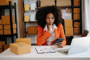 Başlangıçta küçük işletme KOBİ 'si, Girişimci sahibi Afrikalı kadın dizüstü bilgisayar kullanıyor ve paket ürün kutularını hazırlamak için online alışveriş siparişlerini kontrol ediyor. ev ofisinde.