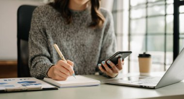İş kadını ofiste dizüstü bilgisayar, telefon ve mali grafiklerle oturuyor