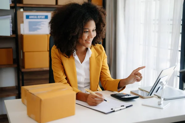 stock image Small business entrepreneur SME freelance African woman working at home office with tablet pc and boxes