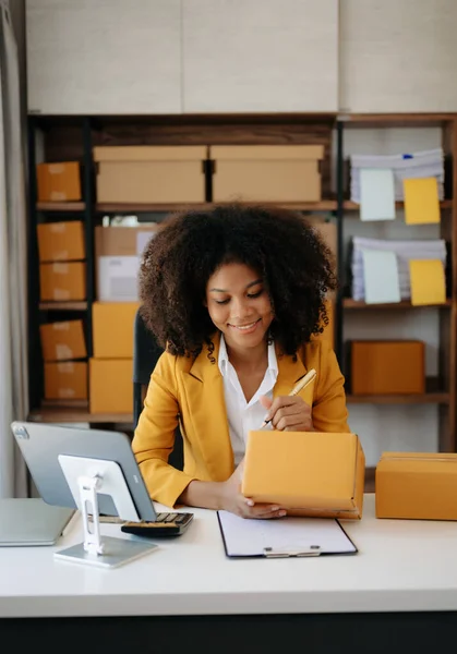 stock image Small business entrepreneur SME freelance African woman working at home office with tablet pc and boxes