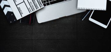 Movie clapper, laptop, tablet, not defteri ve belgelerle modern masaüstü görüntüsü olan ofis malzemeleri..