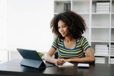  Güzel Afrikalı kadın çalışma yerinde otururken tablet ve hesap makinesi kullanıyor. Ofise odaklanmış.