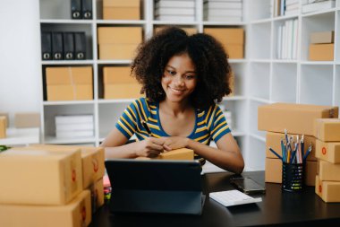 Küçük işletme girişimcisi KOBİ Serbest çalışan Afrikalı kadın ev ofisinde kutu ve tabletle çalışıyor, e-ticaret konsepti
