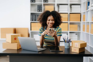 Küçük işletme girişimcisi KOBİ 'li serbest çalışan Afrikalı kadın ev ofisinde kutu ve dizüstü bilgisayarlı telefon ve e-ticaret konseptiyle çalışıyor