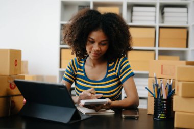 Küçük işletme girişimcisi KOBİ Serbest çalışan Afrikalı kadın ev ofisinde kutu ve tabletle çalışıyor, e-ticaret konsepti